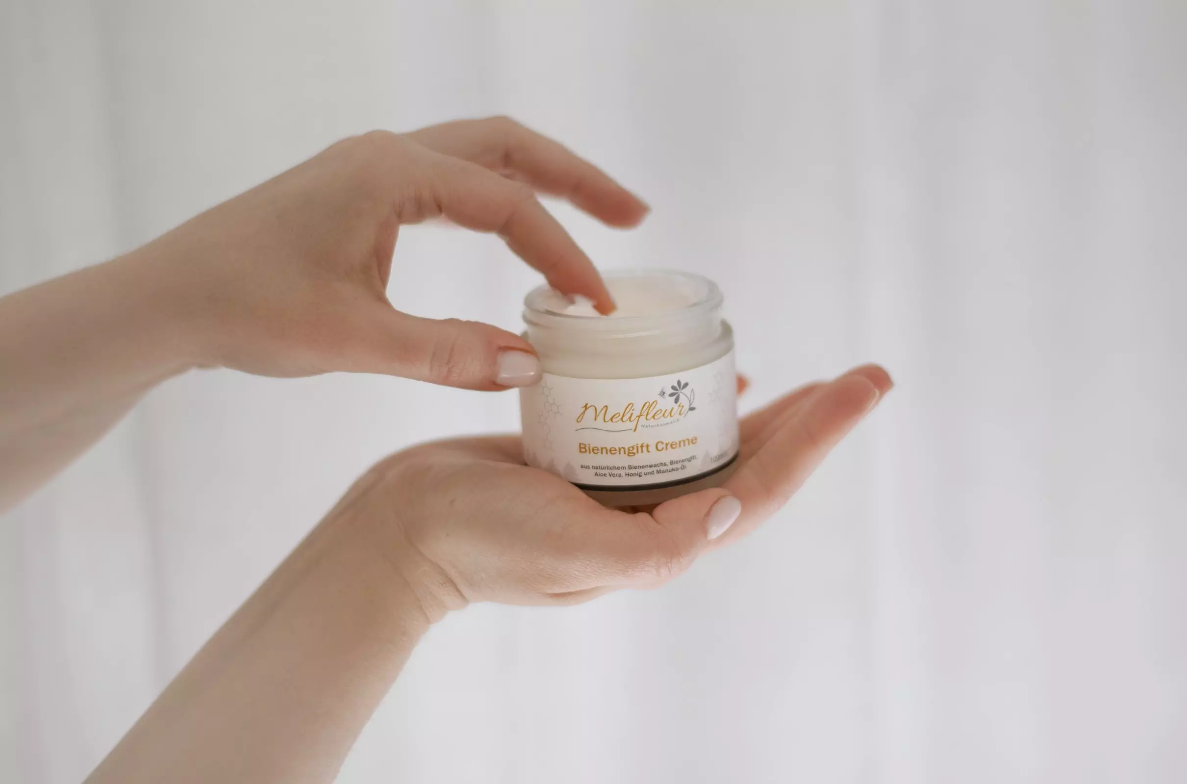 Eine Person hält ein Glas Melifera Bienenfett Creme in einer Hand und schöpft mit der anderen Hand etwas Creme mit den Fingern heraus.