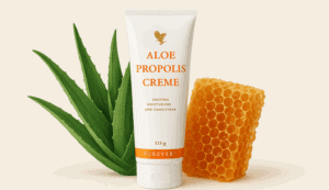 Eine Tube Aloe Propolis Creme steht aufrecht zwischen einem Aloe-Vera-Blatt und einer Honigwabe vor einem hellen Hintergrund.